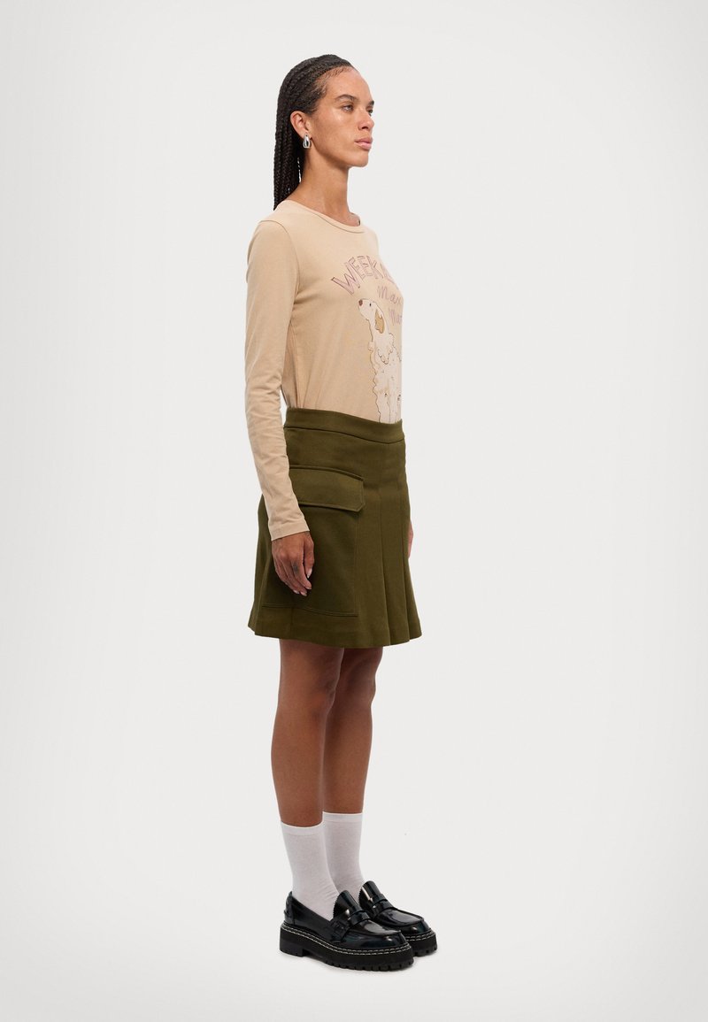 Beige langermet skjorte med sauemotiv, olivengrønn knelang skjørt med frontlommer, hvite sokker og svarte platåsko.