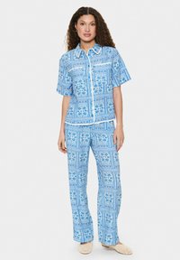 Modrý súbor s krátkym rukávom a širokými nohavicami, s kvetinovými vzormi a bielymi akcentmi, vyrobený z ľahkého materiálu.