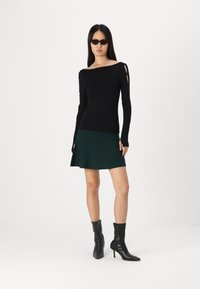 Tricou negru cu mâneci lungi, cu un design off-shoulder și fante pe mâneci, asortat cu o fustă verde evazată și cizme negre până la gleznă.
