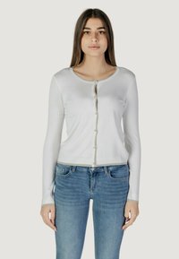 Cardigan bianco a maniche lunghe con scollatura rotonda, chiusura con bottoni argentati e orlo a contrasto. Abbinato a jeans azzurri chiari. Texture liscia.