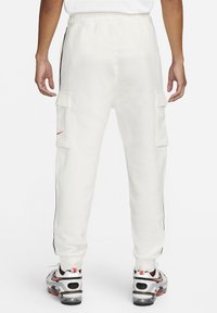 White cargo joggers with black side stripes, elastic waistband, and two side pockets. Worn with multicolored sporty shoes.