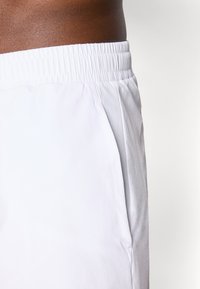 Hvite treningsshorts med elastisk livlinje, sidelommer og en jevn tekstur. Designet for komfort og bevegelsesfrihet.