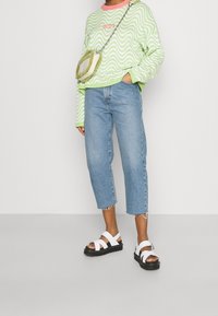 Zielony sweter w falowany wzór, jasnoniebieskie, krótkie dżinsy z postrzępionymi końcami oraz białe sandały na paski z czarnymi podeszwami. Mała zielona torebka na ramię.