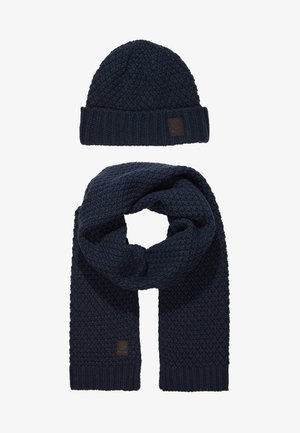 Conjunto de gorro y bufanda de punto de color azul marino, con un patrón texturizado y un parche de cuero en el gorro, con bordes acanalados para mayor calidez.
