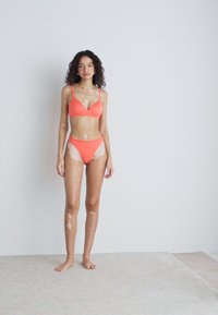 Koraal bikini set met een driehoekige bralette en low-rise slipje. Glad materiaal met verstelbare bandjes en minimale stiksels.