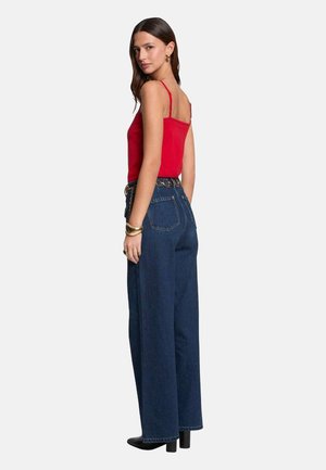 Un haut rouge à bretelles spaghetti associé à un jean bleu foncé taille haute et ample. Le jean possède des poches arrière et une ceinture avec des accents métalliques.