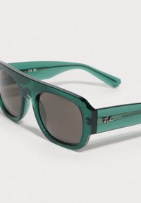 Óculos de sol de plástico verde com uma armação espessa, lentes escuras e logótipo Ray-Ban na lateral. Apresenta um acabamento suave e brilhante.