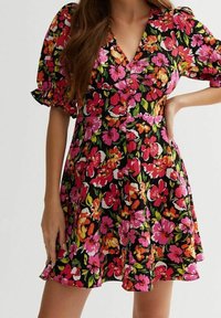 Robe florale avec un fond noir et des fleurs vibrantes roses, oranges et vertes. Manches courtes à volants et décolleté en V.