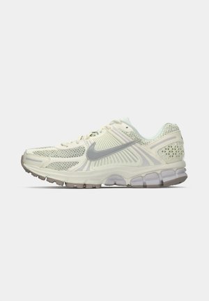 Sneakers atletice de culoare bej deschis, cu materiale din plasă și sintetice, o talpă intermediară texturată și accente gri pe swoosh și călcâi.