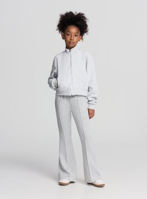 Felpa grigia con zip, collo alto e design corto, abbinata a pantaloni della tuta grigi a zampa con cuciture verticali e tessuto morbido.