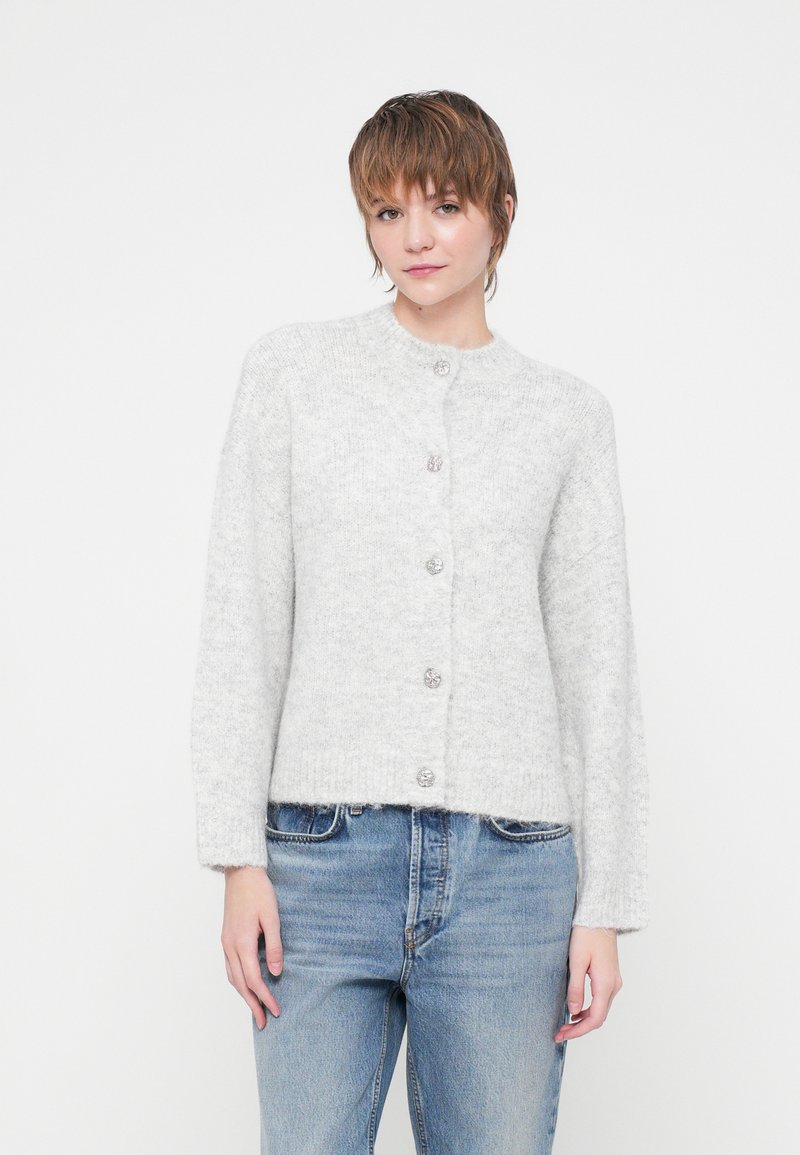 Cardigan grigio chiaro in maglia morbida e pelosa con colletto rotondo e sette bottoni metallici frontalmente. Maniche lunghe e vestibilità cropped.