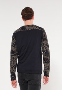 Męska bluza z ciemnoniebieskim korpusem i brązowymi rękawami z abstrakcyjnym wzorem. Wykonana z miękkiego materiału, z prążkowanymi mankietami i ściągaczem w talii.