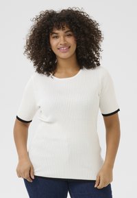 Witte geribde gebreide top met korte mouwen en zwarte contrasterende accenten bij de manchetten en zoom, gedragen met blauwe denim jeans.