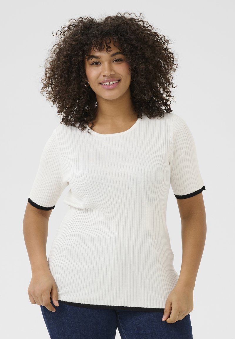 Witte geribde gebreide top met korte mouwen en zwarte contrasterende accenten bij de manchetten en zoom, gedragen met blauwe denim jeans.