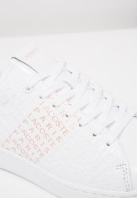 Biała sneakersy Lacoste z wytłoczonym napisem "LACOSTE PARIS" w jasnoróżowym kolorze, białe sznurowadła i gładki skórzany materiał.