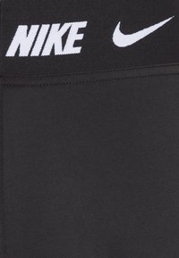 Leggings sportive negre cu un talie largă, având inscripționarea albă "NIKE" și un logo Swoosh alb mai mic. Textură de material neted.