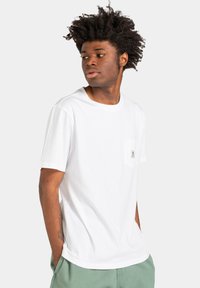 Hvid bomulds t-shirt med rund hals og korte ærmer. Har en lille brystlomme med et mærke. Glat tekstur og afslappet pasform.