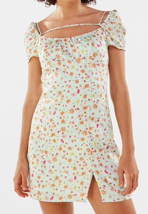 Woman wearing a light floral mini dress with puff sleeves, a square neckline, and a front thigh-high slit.