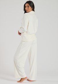 Witte loungewear set bestaande uit een langarm T-shirt met kraag en brede broekspijpen, gemaakt van zachte stof; eenvoudig, minimalistisch ontwerp.
