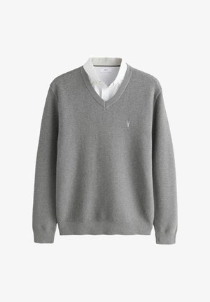 Grau gestrickter Pullover mit V-Ausschnitt, strukturiertem Stoff und kleinem Logo auf der linken Brust, getragen über einem weißen Hemd mit Kragen.