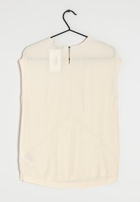 Sleeveless cream blouse with a round neckline, back keyhole opening, soft texture, and a slightly curved hem. Hangs on a black hook.