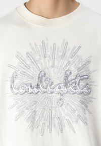 Hvid bomulds t-shirt med et sølvfarvet grafisk design, der fremhæver ordet "coulights" omgivet af stråler, der ligner solstråler.