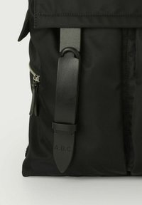Zaino nero con un esterno in tessuto liscio, una spalla regolabile evidente e una piccola tasca con zip dettagliata in hardware argentato.