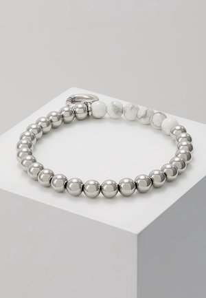 Bracelet avec des perles en argent poli alternant avec des perles en pierre marbrée blanche, posé sur un socle gris, avec un fermoir en argent.