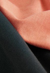 Twee stofstalen: één in zacht koraal en één in gestructureerd zwart, die zowel gladde texturen als subtiele breipatronen tonen.