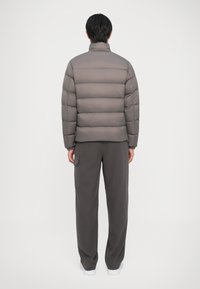 Šedá puff jacket s horizontálnymi švami, vysokým golierom a elastickými manžetami, skombinovaná s ladiacimi šedými nohavicami so bočnými vreckami.