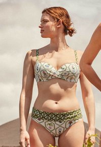 Bikini verde y blanco con un top estructurado y envuelto y parte inferior de talle alto; diseños florales y geométricos; textura de tela suave.