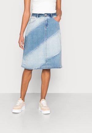 Jupe en denim en forme A avec un bloc de couleur diagonale allant du bleu clair au bleu moyen, dotée de poches et d'une taille à boutons, associée à des baskets claires.