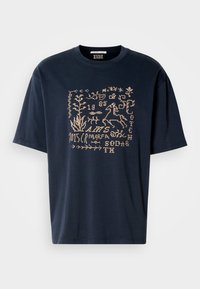 Μπλε βαμβακερό T-shirt με ελαφρύ μπεζ γραφικό σχέδιο που περιλαμβάνει φυτά και ζώα, όπως ένα άλογο, και στοιχεία κειμένου. Στρογγυλή λαιμόκοψη.