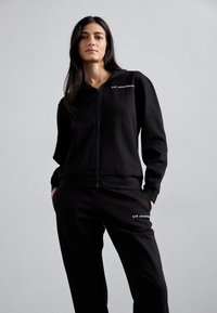 Zwarte ritssluiting hoodie met bijpassende joggers, vervaardigd uit zachte, gestructureerde stof. Bevat wit merklogo op beide stukken. Strak design.