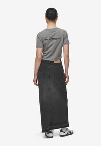 Grå kortärmad t-shirt med texten "INGEN HASTIGHETSRÄTT" på baksidan, tillsammans med en lång svart jeanskjol och vit och svart sneakers.