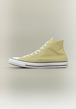 Zapatilla alta de lona color amarillo claro con puntera de goma blanca, cordones blancos y suela blanca con rayas negras, mostrada en perfil lateral.