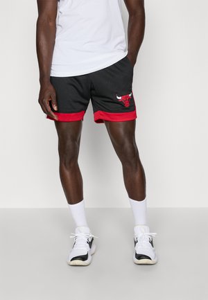 Melni tīkla šorti ar sarkaniem akcentiem un Čikāgas Bulls logo kreisajā kājā. Nēsāti ar baltu T-kreklu un baltām zeķēm, apvienoti ar sporta apaviem.