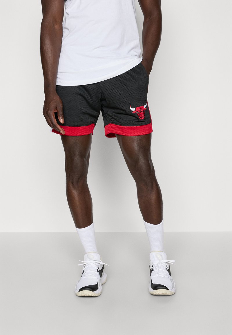 Shorts en mesh noir avec des accents rouges et un logo des Chicago Bulls sur la cuisse gauche. Portés avec un t-shirt blanc et des chaussettes blanches, associés à des baskets.