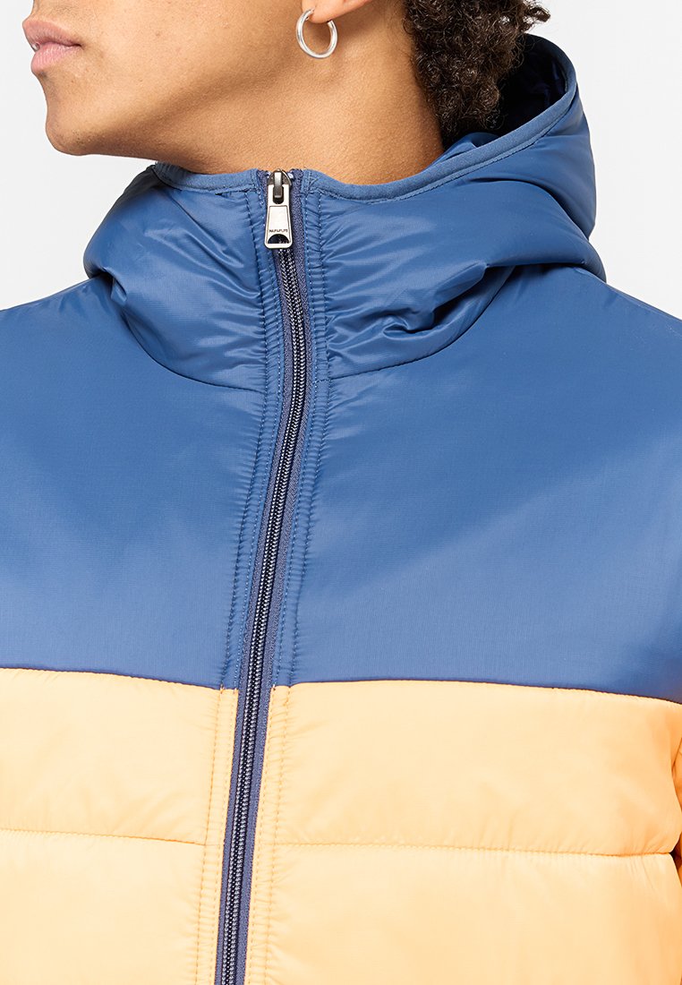 Giacca imbottita con parte superiore blu e parte inferiore gialla. Presenta un colletto alto, chiusura con zip e una texture in tessuto liscia e lucida.
