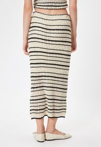 Gonna a maglia con strisce verticali nere e crema, con una texture a coste, che arriva a metà polpaccio, abbinata a ballerine di colore chiaro.