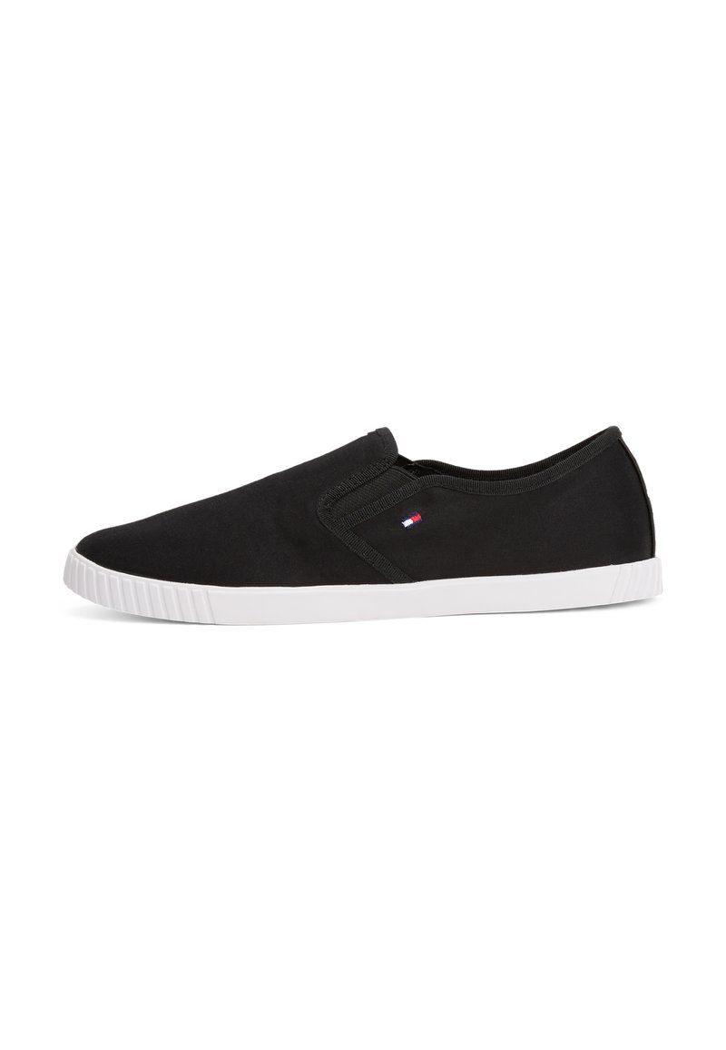 Sorte slip-on sko laget avCanvas-materiale med hvit gummisåle og en liten logo-detalj på siden. Jevn tekstur og strømlinjeformet design.