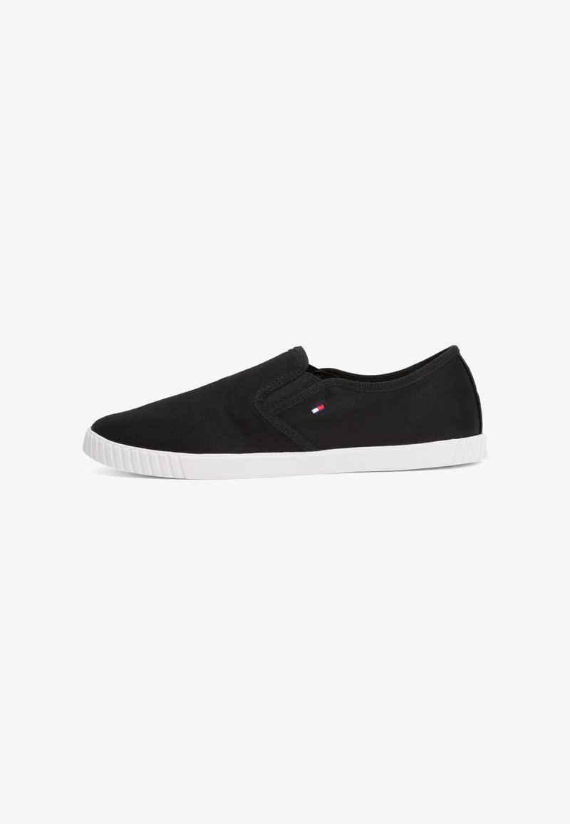 Fekete vászon anyagból készült slip-on cipők, fehér gumitalppal és egy kis logó részlettel az oldalon. Simává és letisztulttá varázsolja a megjelenést.