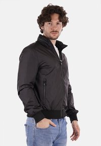 Giacca bomber nera con colletto alto, chiusura a zip anteriore, tasche laterali, polsini a costine e una texture di tessuto liscia e lucida.