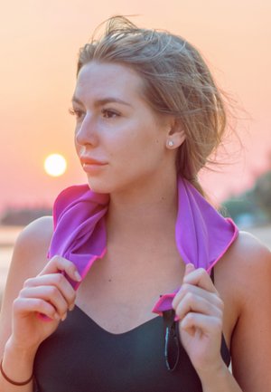 Magenta cooling towel worn around neck, made of lightweight fabric with pink trim, against a sunset backdrop. Smooth texture and vibrant color.