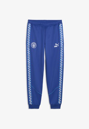 Pantalon de sport bleu Nike avec poignets élastiques, rayures à motifs sur les côtés, logo de Manchester City sur la cuisse gauche, logo Puma et "KING" sur la cuisse droite.