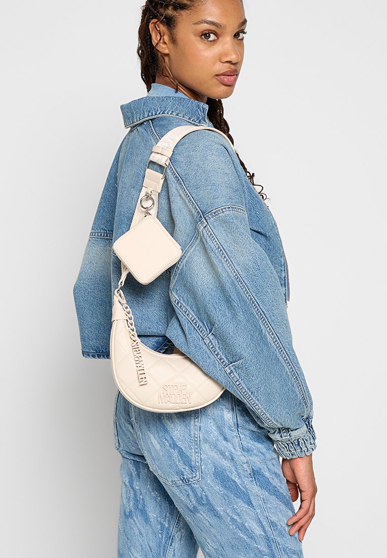 Quilted beige Umhängetasche mit Kettenriemen. Verfügt über einen abnehmbaren, passenden Kartenhalter. Jeansjacke mit lockerer Passform. Blaue Jeans.