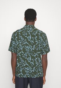 Camicia a maniche corte di colore verde scuro, con una stampa floreale in azzurro chiaro. Realizzata in tessuto morbido con vestibilità rilassata e colletto a bottoni.