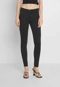 Vaqueros skinny negros con una textura de denim suave, con un diseño de cinco bolsillos y detalles de costura sutiles. Combinados con tacones negros con tiras.