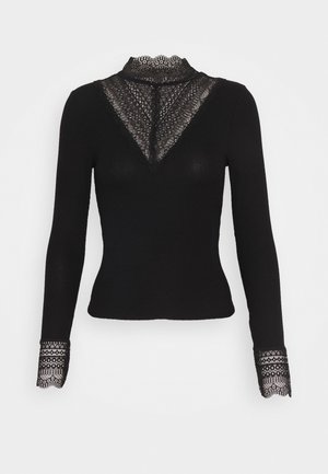 Top noir ajusté à manches longues avec un col montant en dentelle, un détail en V en dentelle sur la poitrine et des poignets en dentelle aux manches.