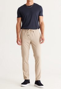 Pantalones jogger beige con cintura elástica, cordón ajustable y bolsillos laterales. Combinados con una camiseta de manga corta azul marino y zapatillas negras.